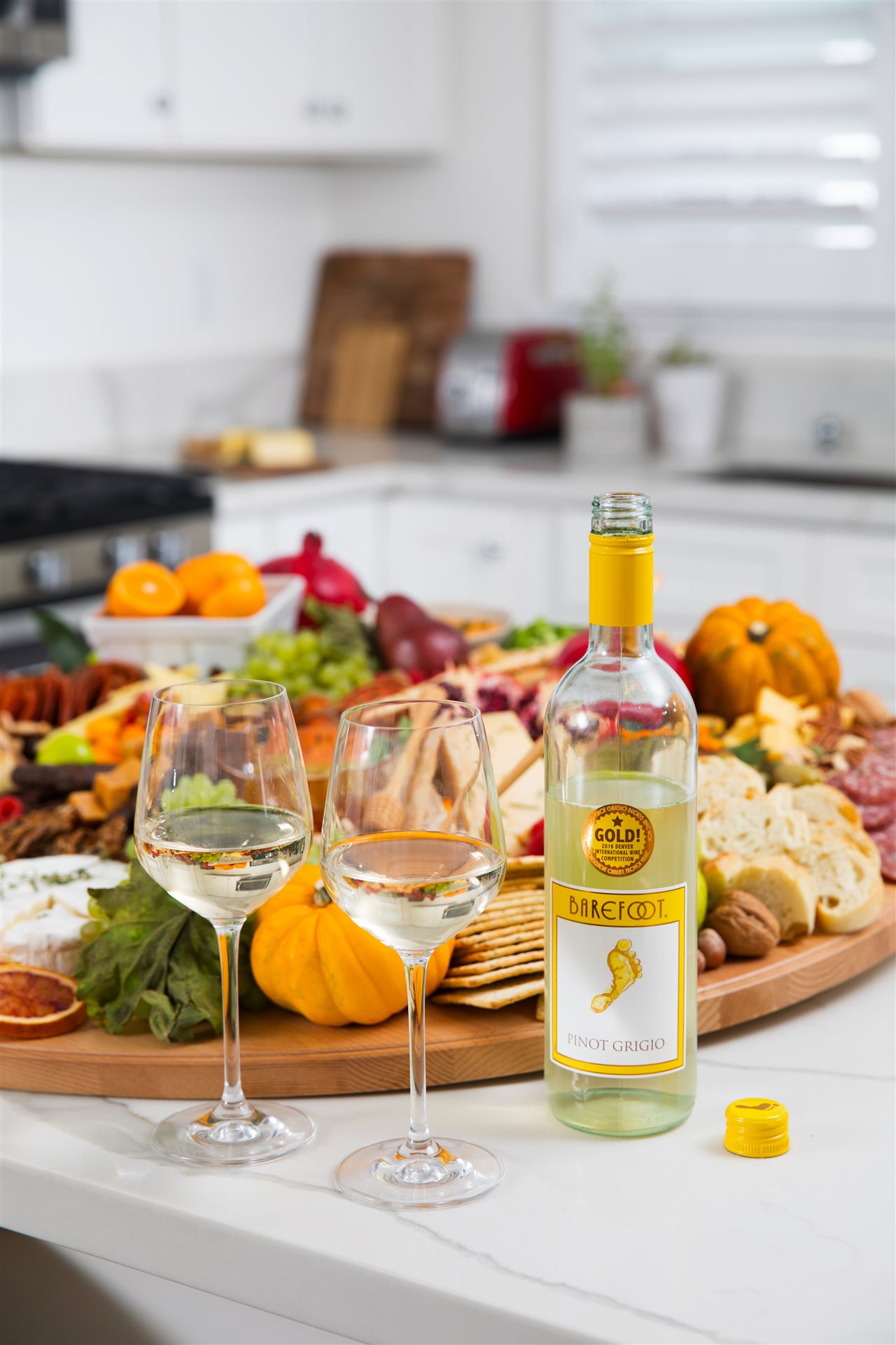 A bottle of barefoot wine and two filled glasses by a huge snack tray.