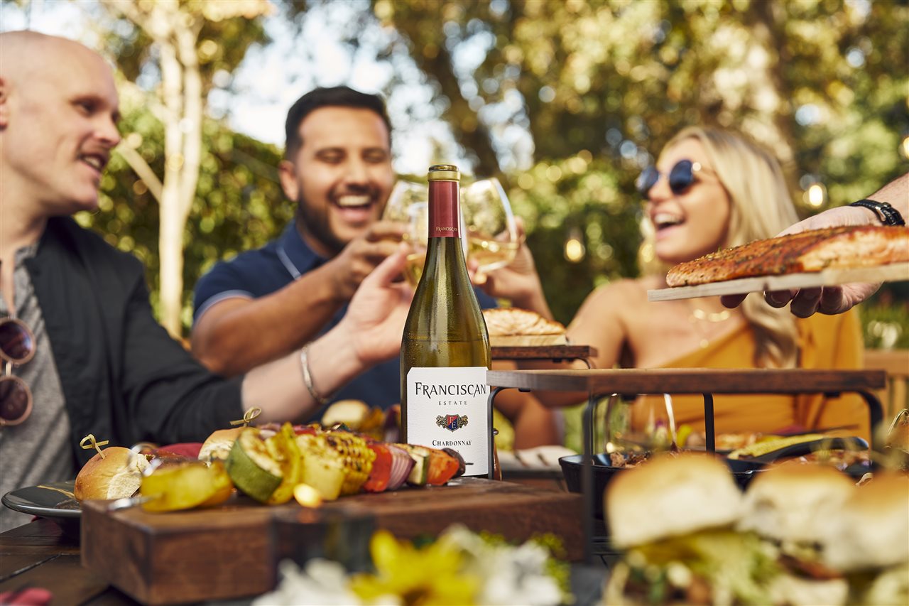 Group of friends enjoying a bottle of wine while having dinner outside.