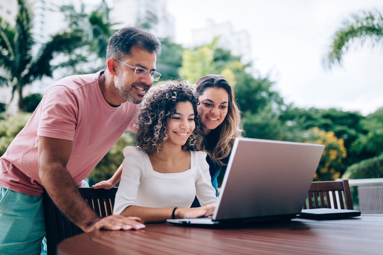 Mom and dad helping college bound daughter answer question on an online form while on their patio.