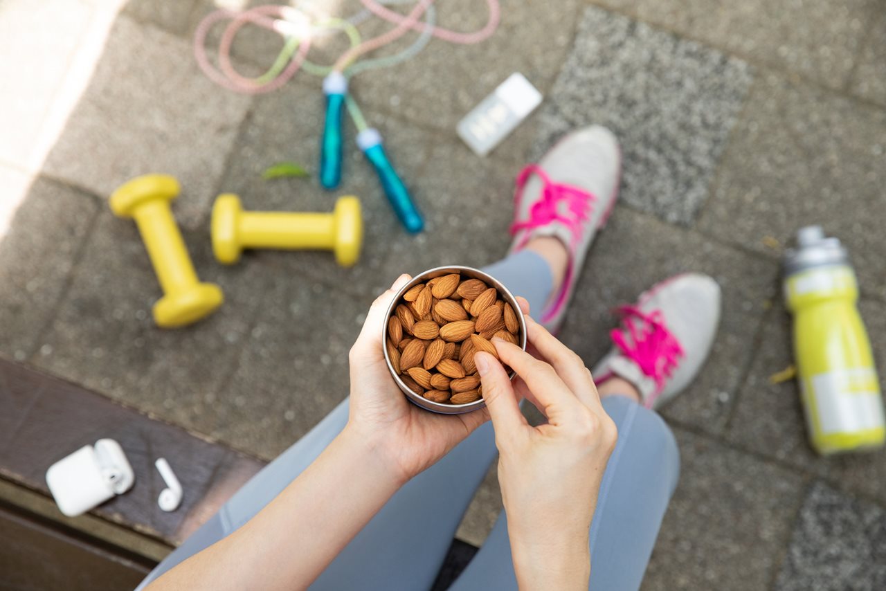 Overhead shot of a woman selecting a nut from a can of almonds with work-out weights jump rope and water bottle near by.