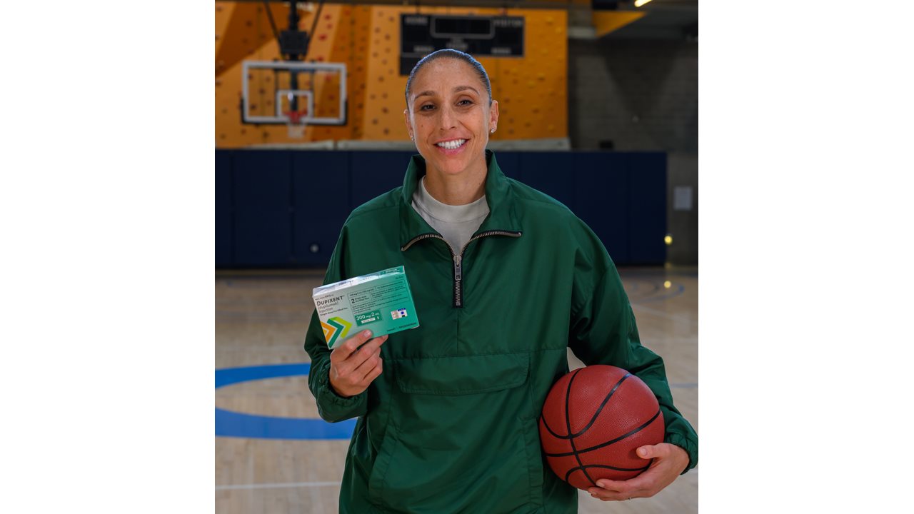 Diane holding a box of medication and a basketball while standing on a basketball court.