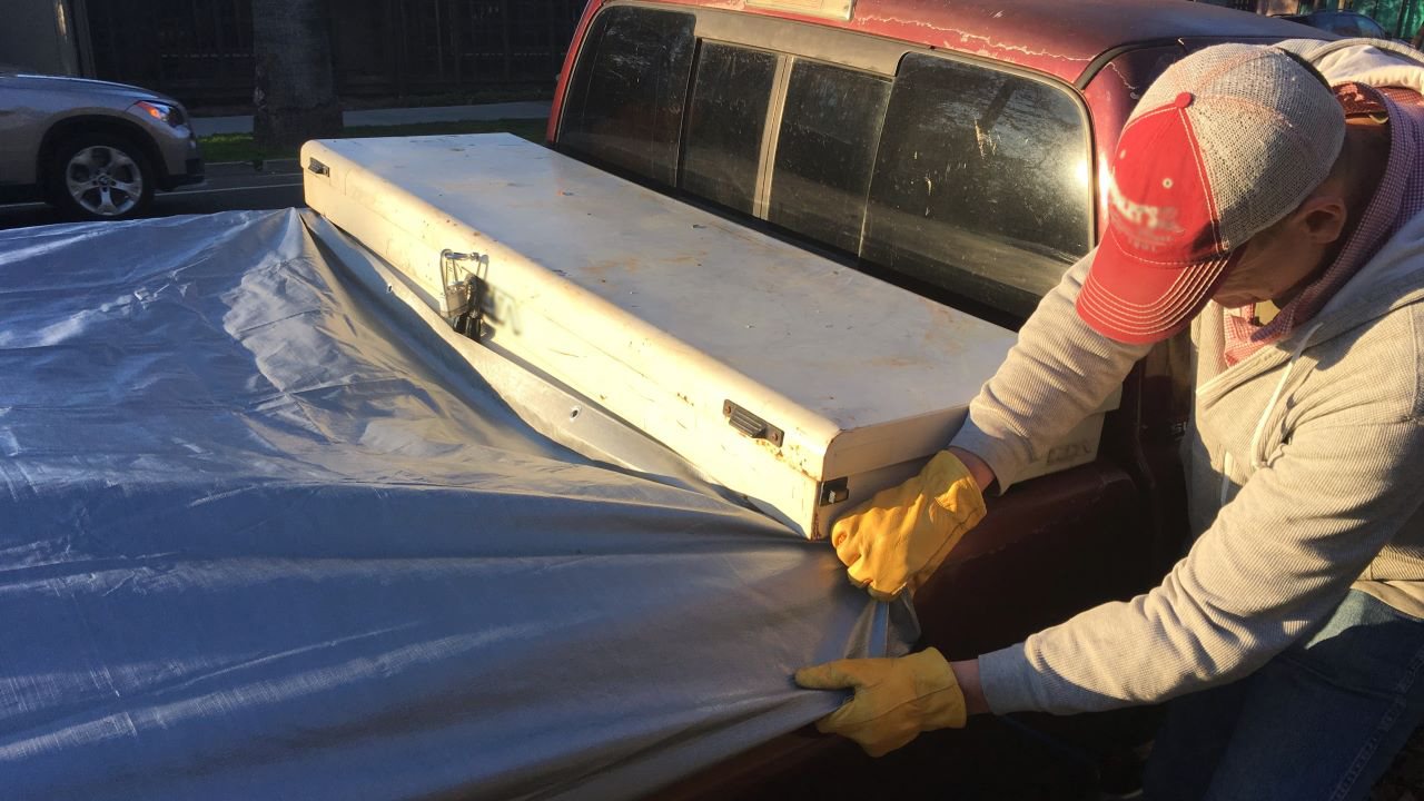 Man securing a load in the back of his pick up with a tarp.