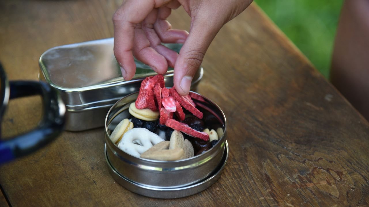 Person loading strawberries and other dried fruits in re-useable tin.