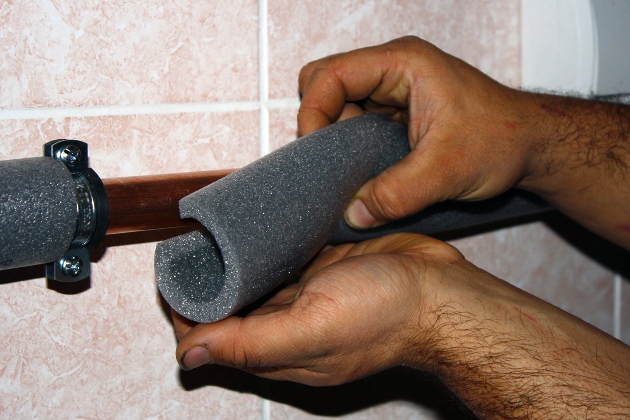 Man putting foam insulations around his pipes.