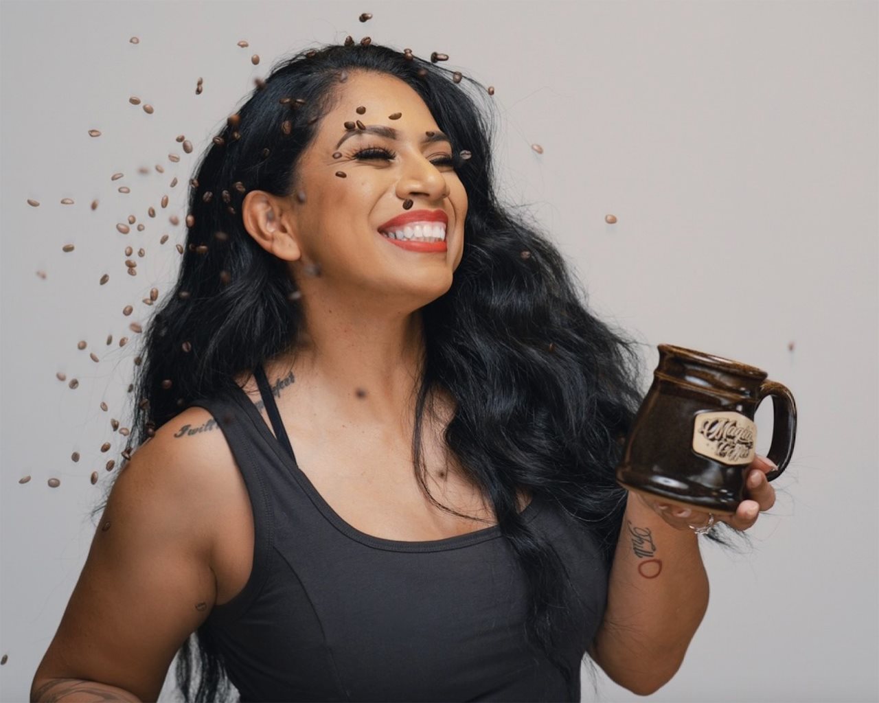 Sgt. 1st Class Elizabeth Calderon wearing a tank top and holding a cup of coffee while coffee beans rain down like confetti.