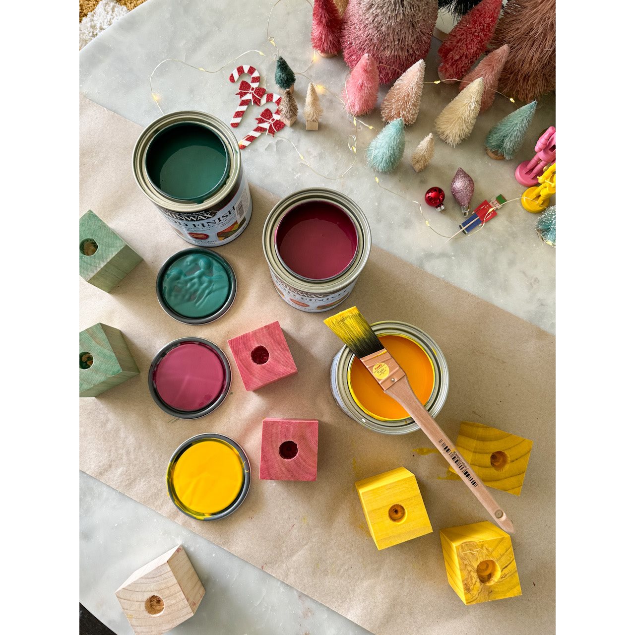 Wooden candle holders and open cans of miniwax stain next to holiday ornaments on the table.