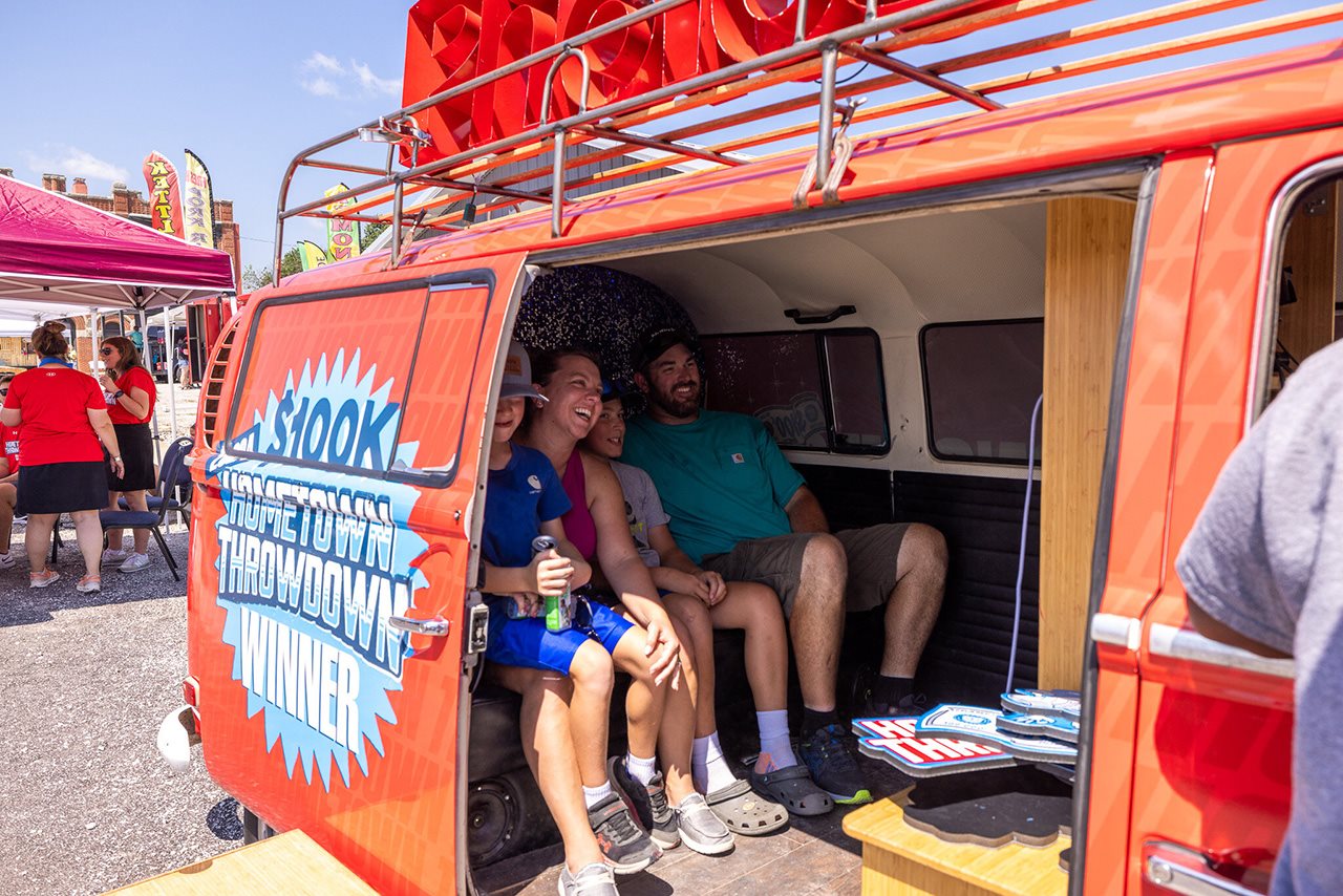 Smiling family sits in a van with a door reading 