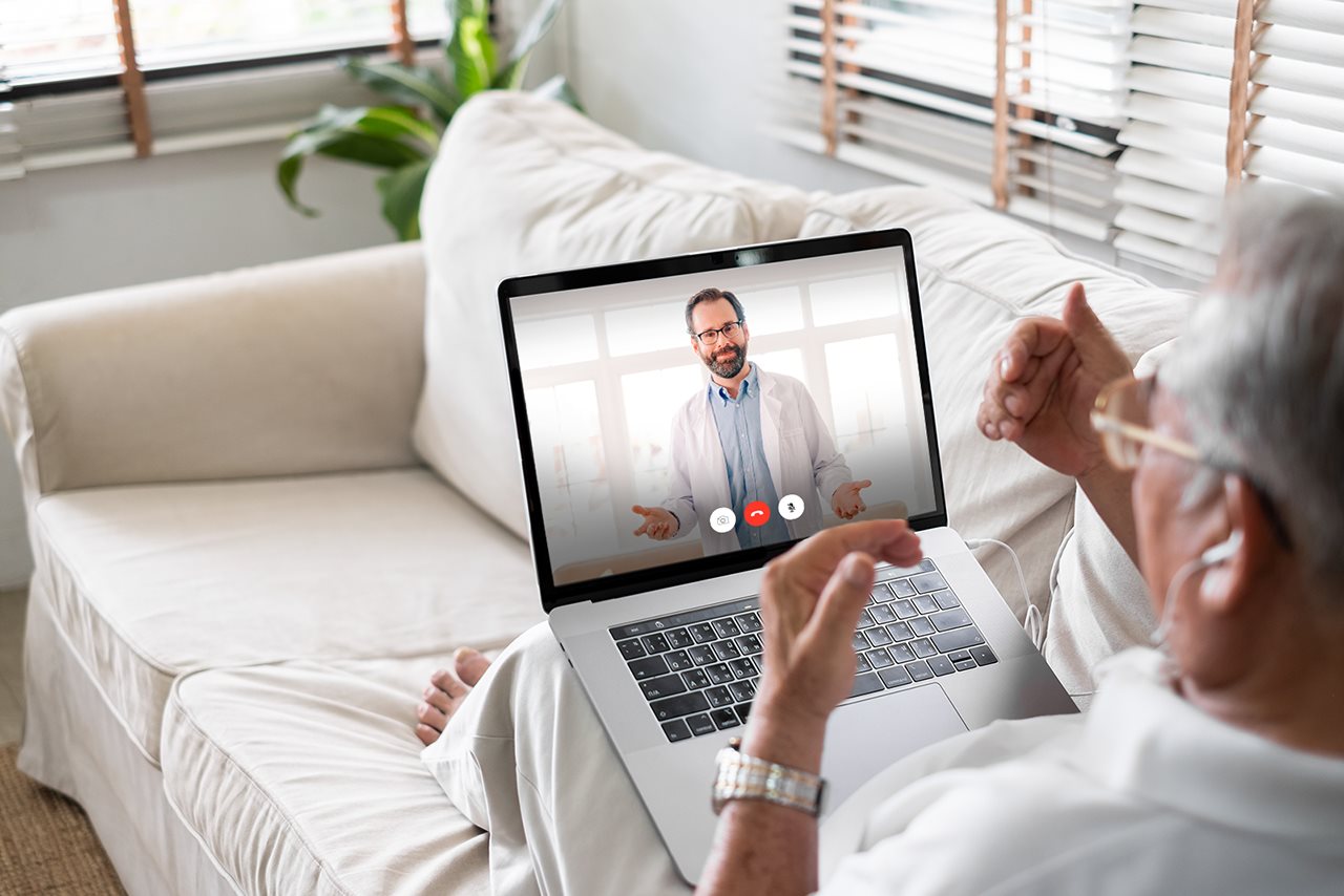 Older man sitting on the couch at home and talking with a doctor in a video chat.