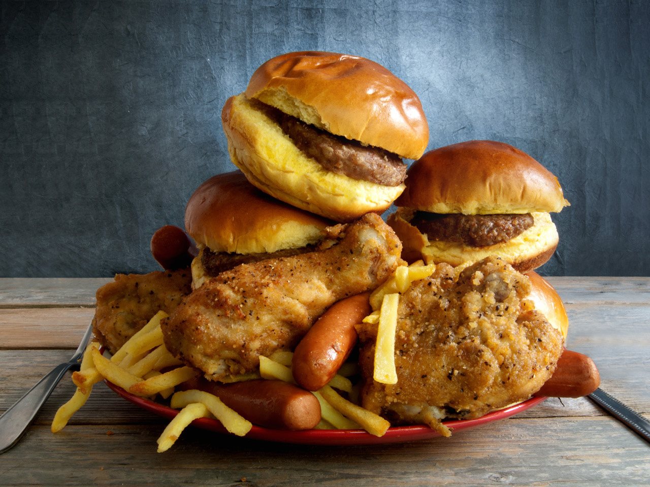 A pile of hamburgers, french fries, fried chicken and hot dogs on a plate.