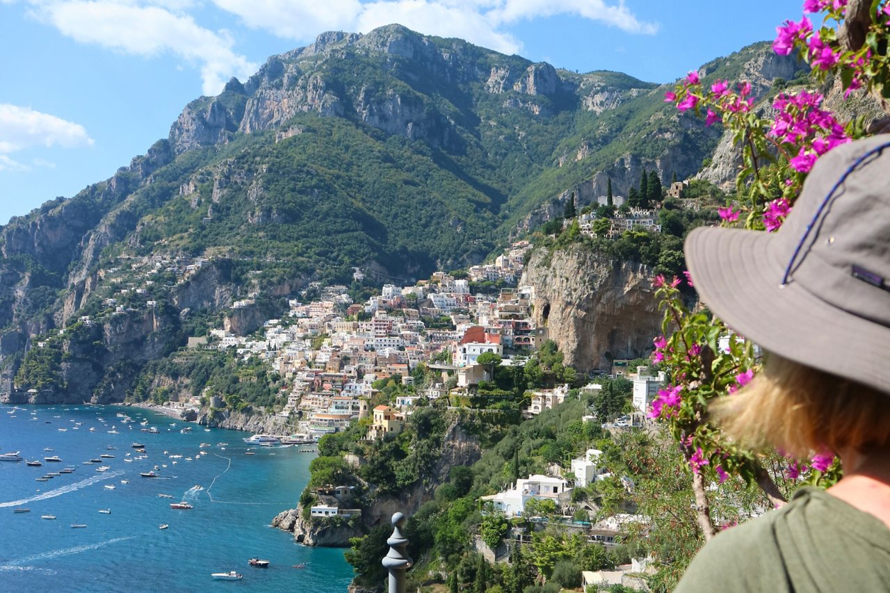 A woman in a sun hat enjoying a view of the Amalfi coast with its terraced homes and other buildings.