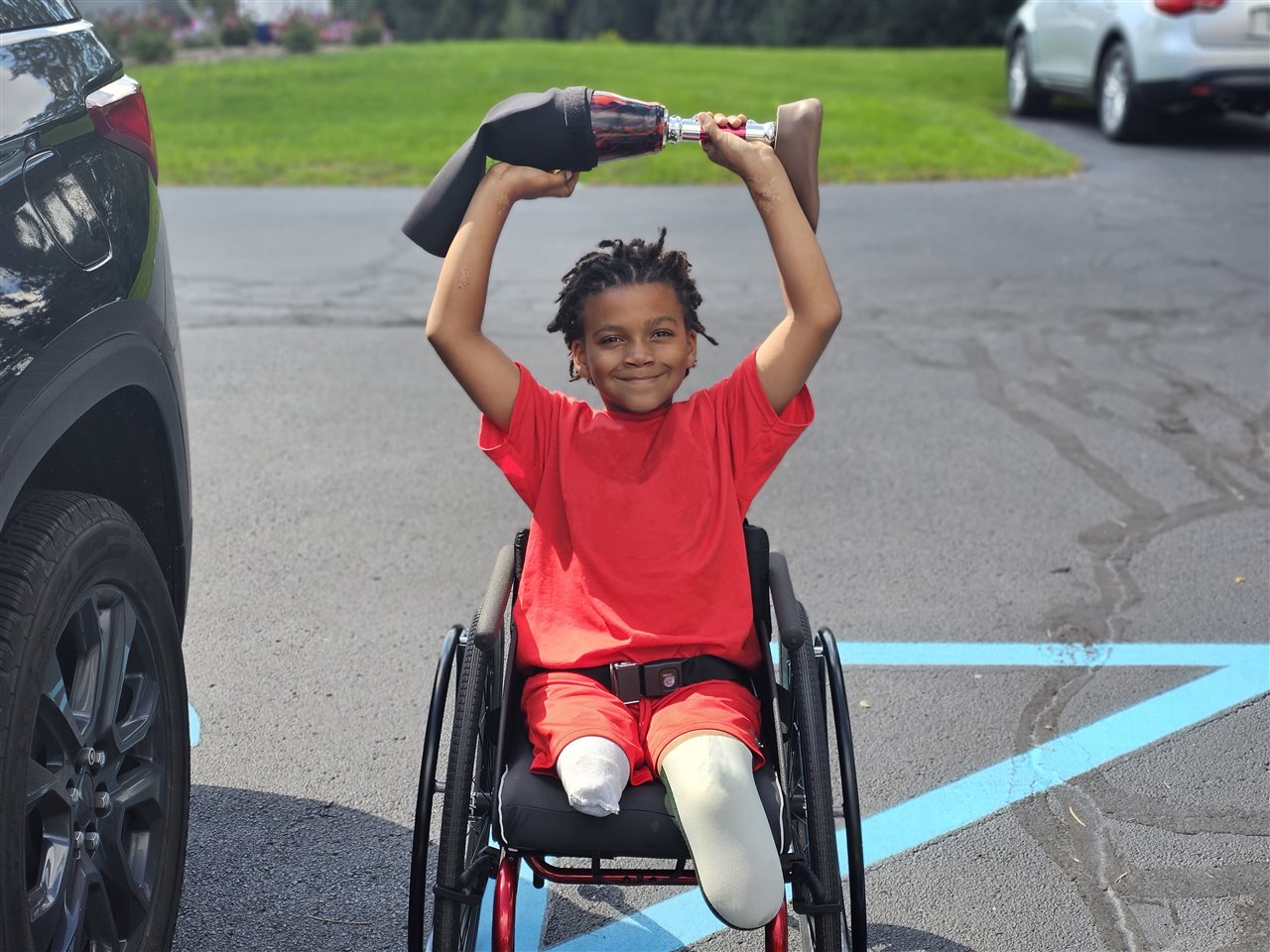 Boy in a wheelchair smiling and holding a prosthetic leg over his head.