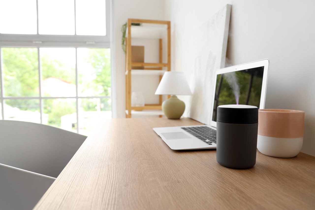 Mini humidifier sitting by a laptop on a desk at home.