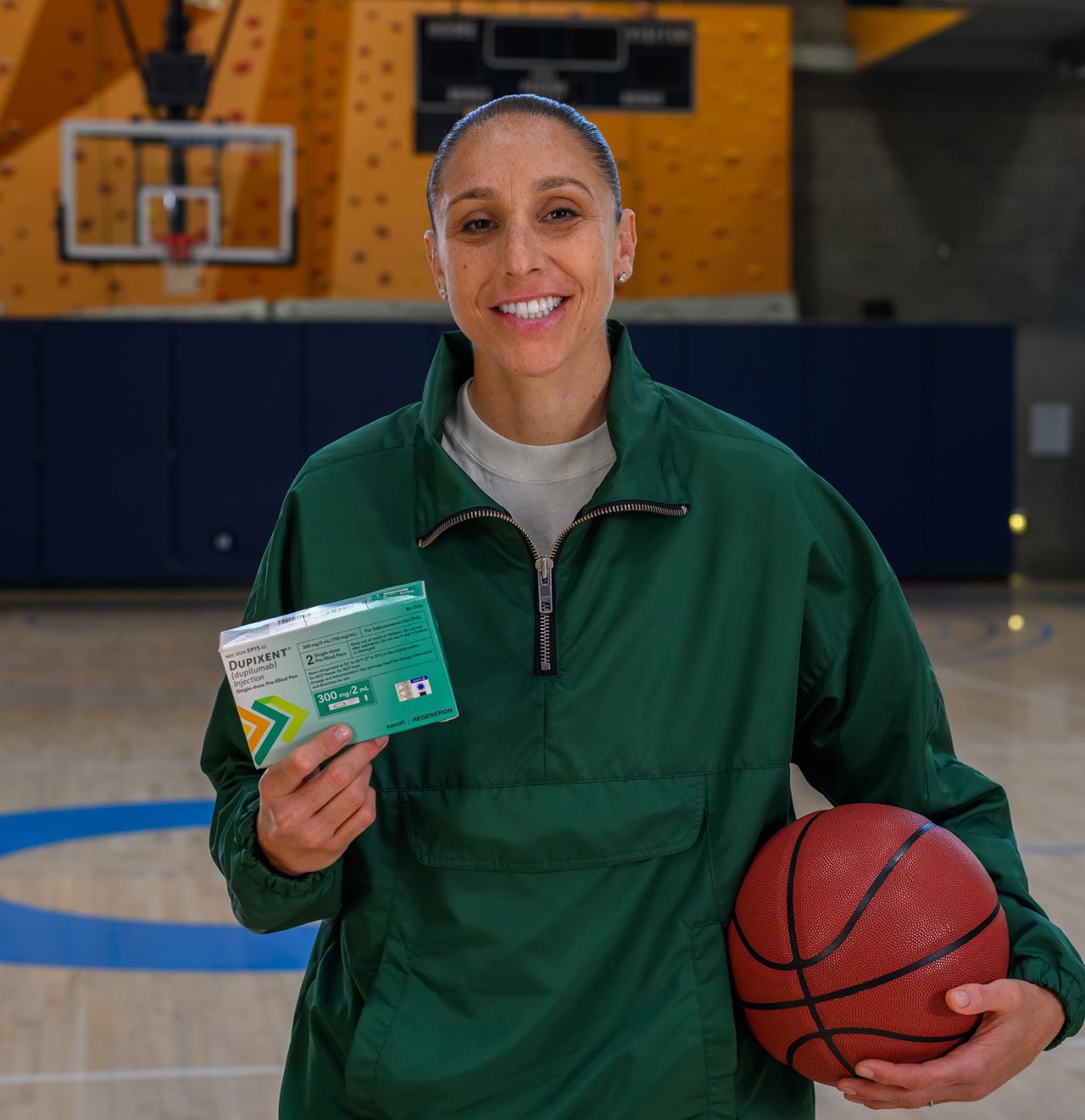 Diane holding a box of medication and a basketball while standing on a basketball court.