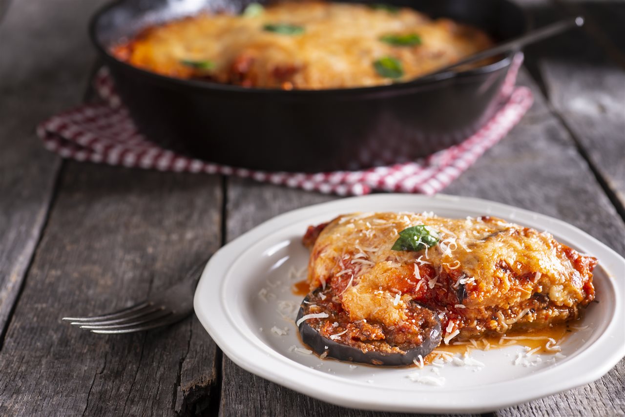 Close up of a plate of Eggplant Parmigiana with cast iron pot in the back ground