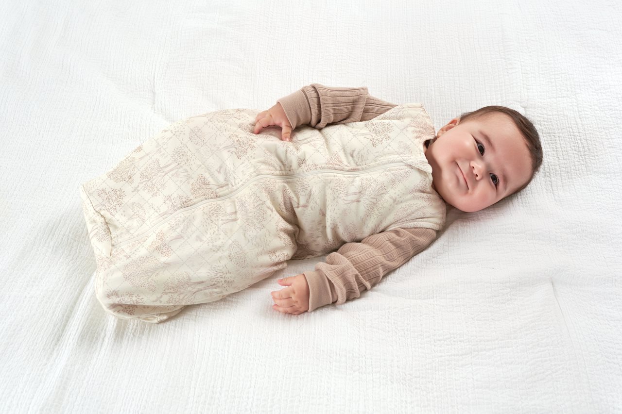 Cute baby suggled up in a cream color wearable blanket.