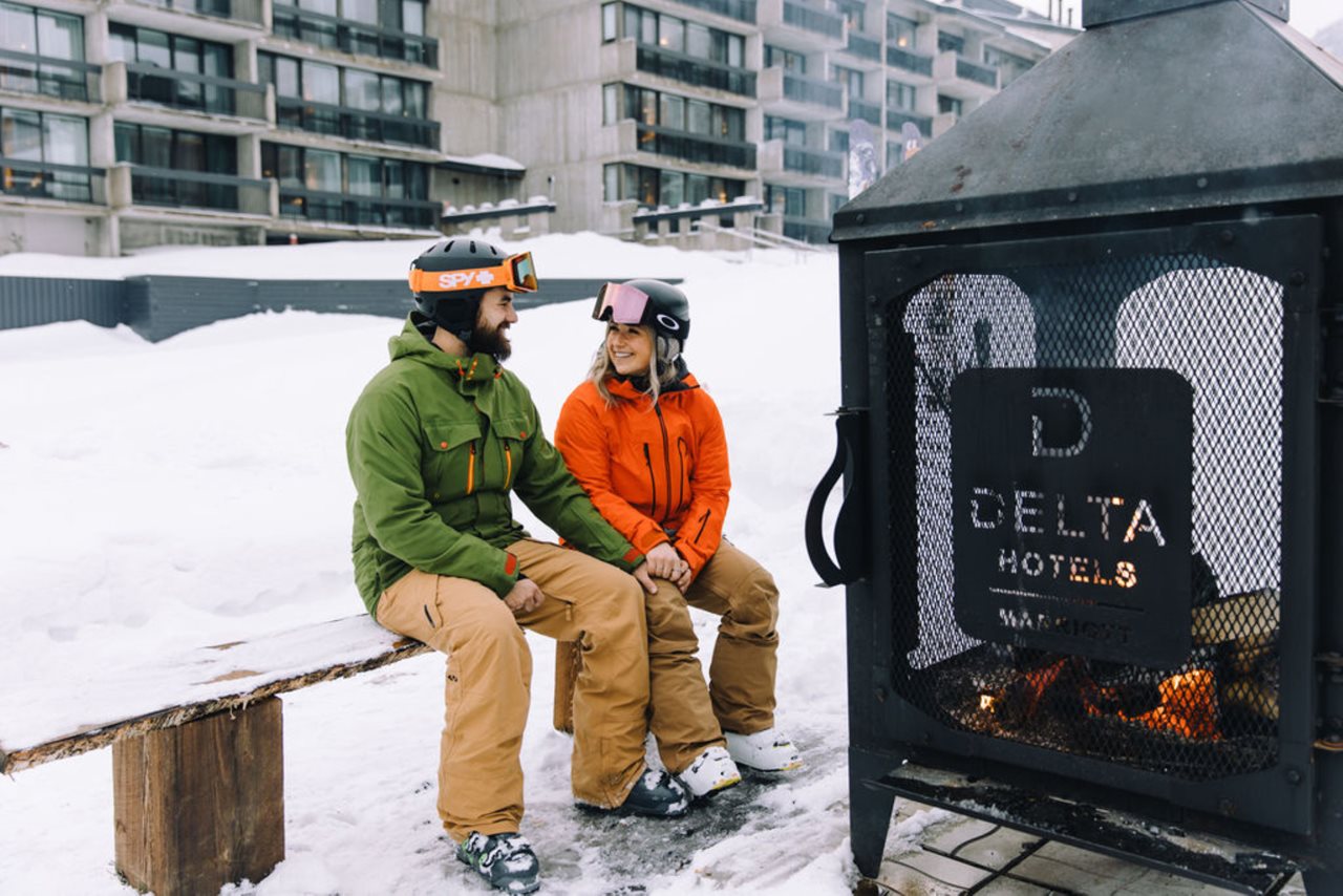 Young couple in ski gear sitting by the outdoor fire afterin sking in to the Delta hotel by Marriott Mont Sainte Anne