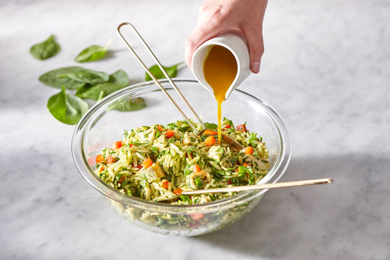 Woman pouring dressing on Chicken salad orzo in a bowl