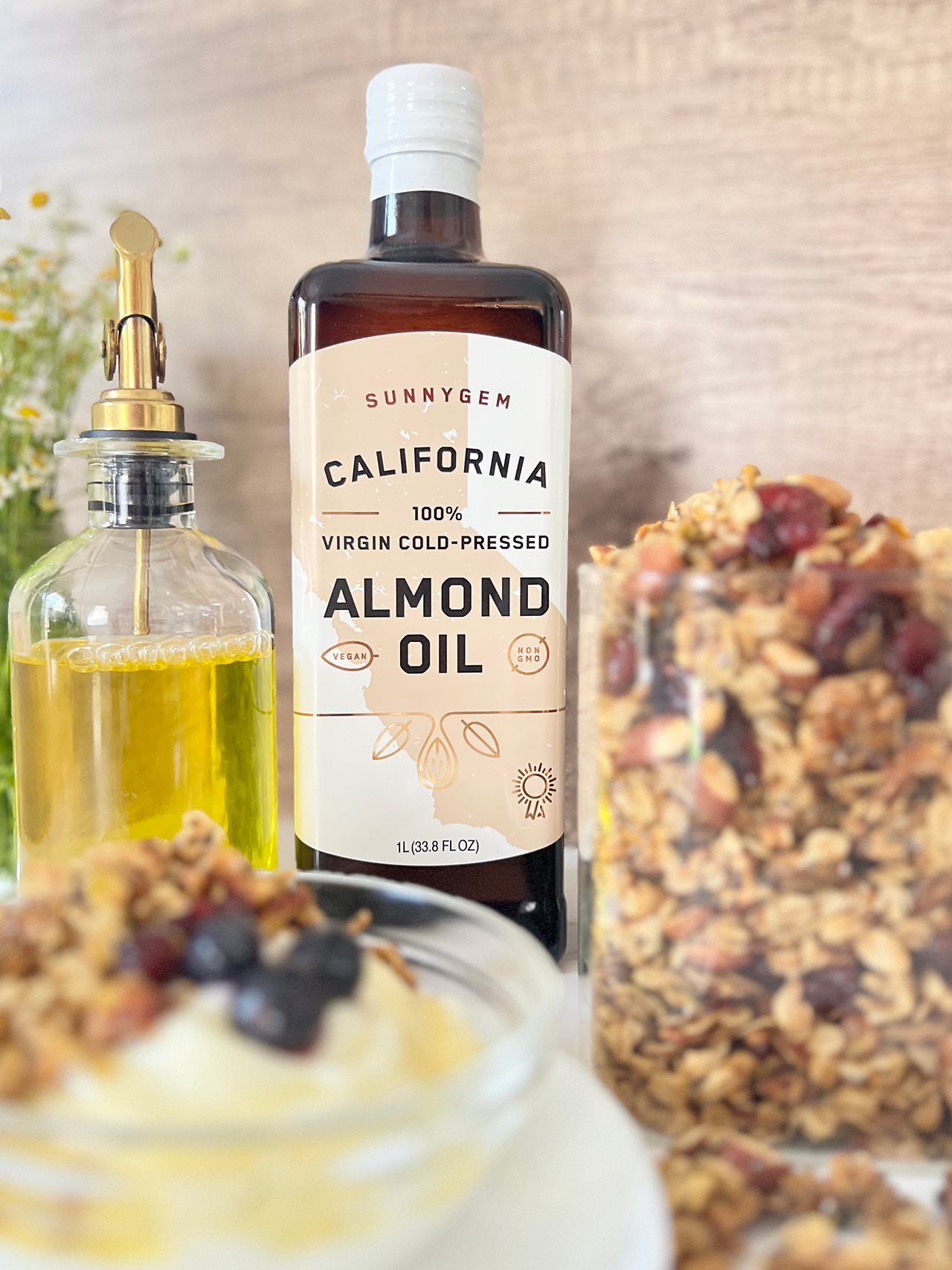 SunnyGem California 100% virgin cold-pressed almond oil with a glass container holding a variety of nuts and dried fruits.