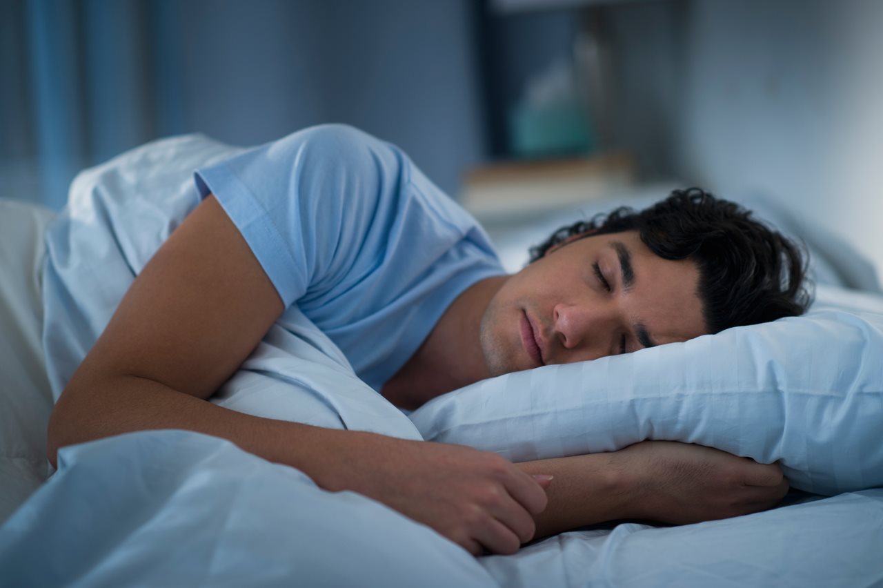 Man wearing a blue t-shirt and sleeping in bed.