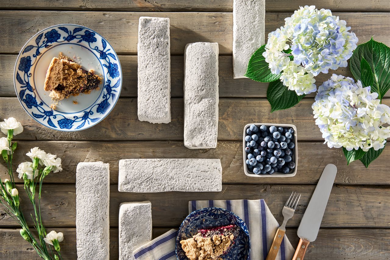 Snowpack handformed bricks on rustic wood table with plates of homemade pie, a basket of blueberries and flowers.