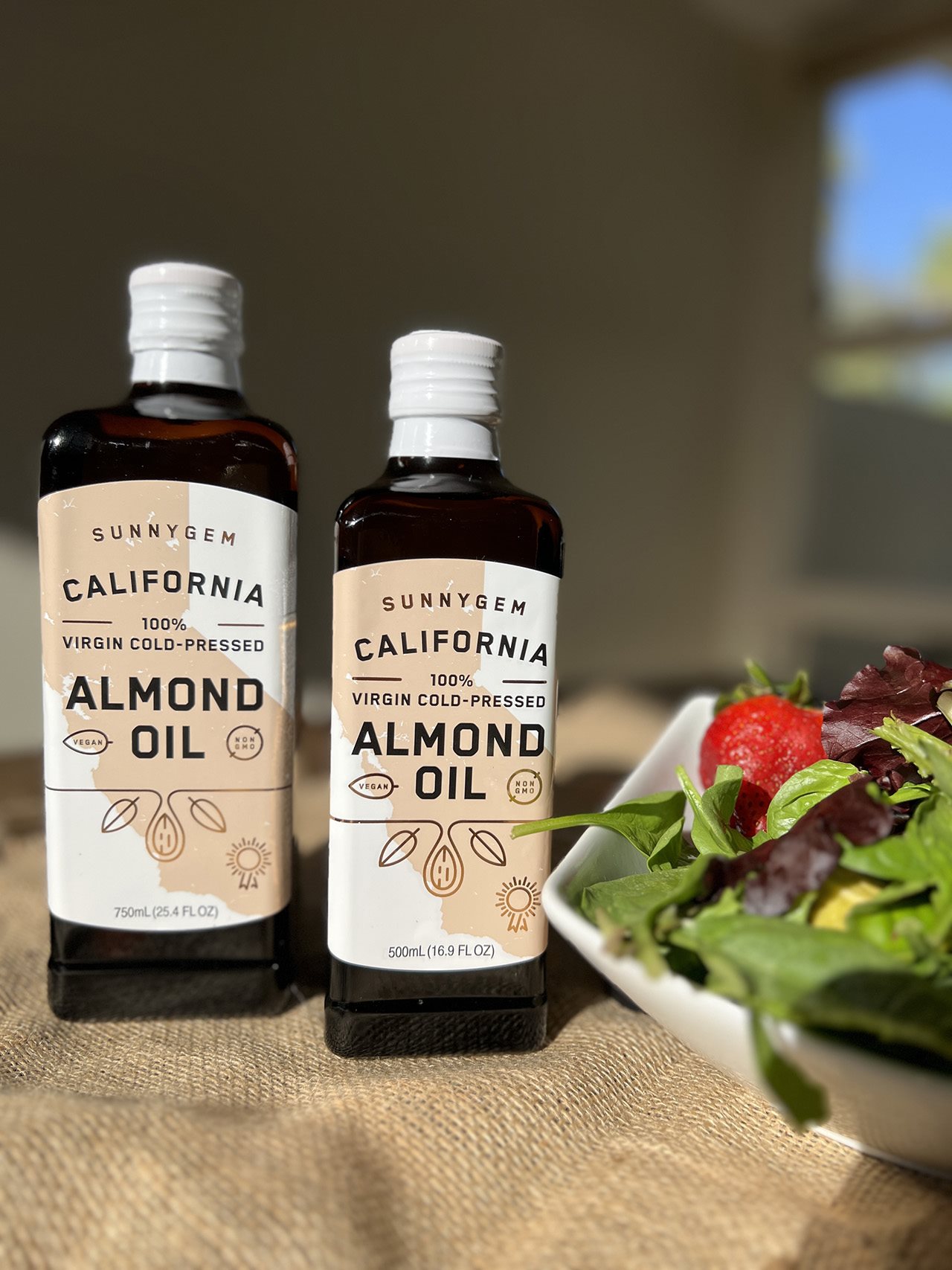 Two bottles of SunnyGem Almond Oil next to a salad.