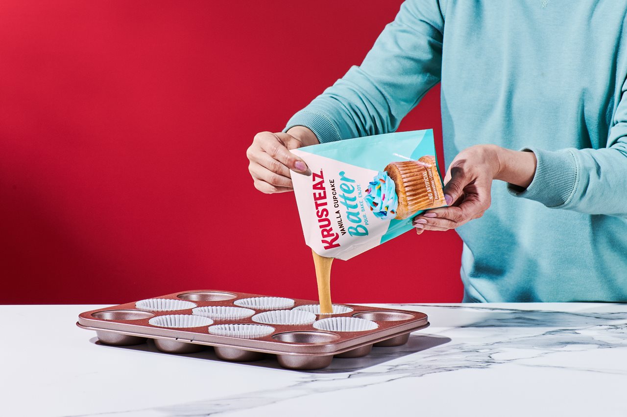 Person pouring a batch of vanilla cupcake batter into a cupcake tin