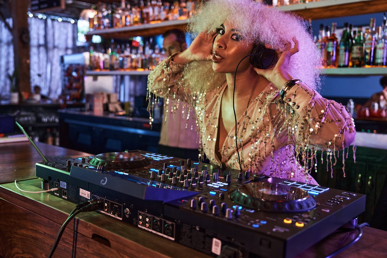 Woman hearing a sparkly outfit and headphones in a bar while using the AlphaTheta XDJ-AZ by pioneer.