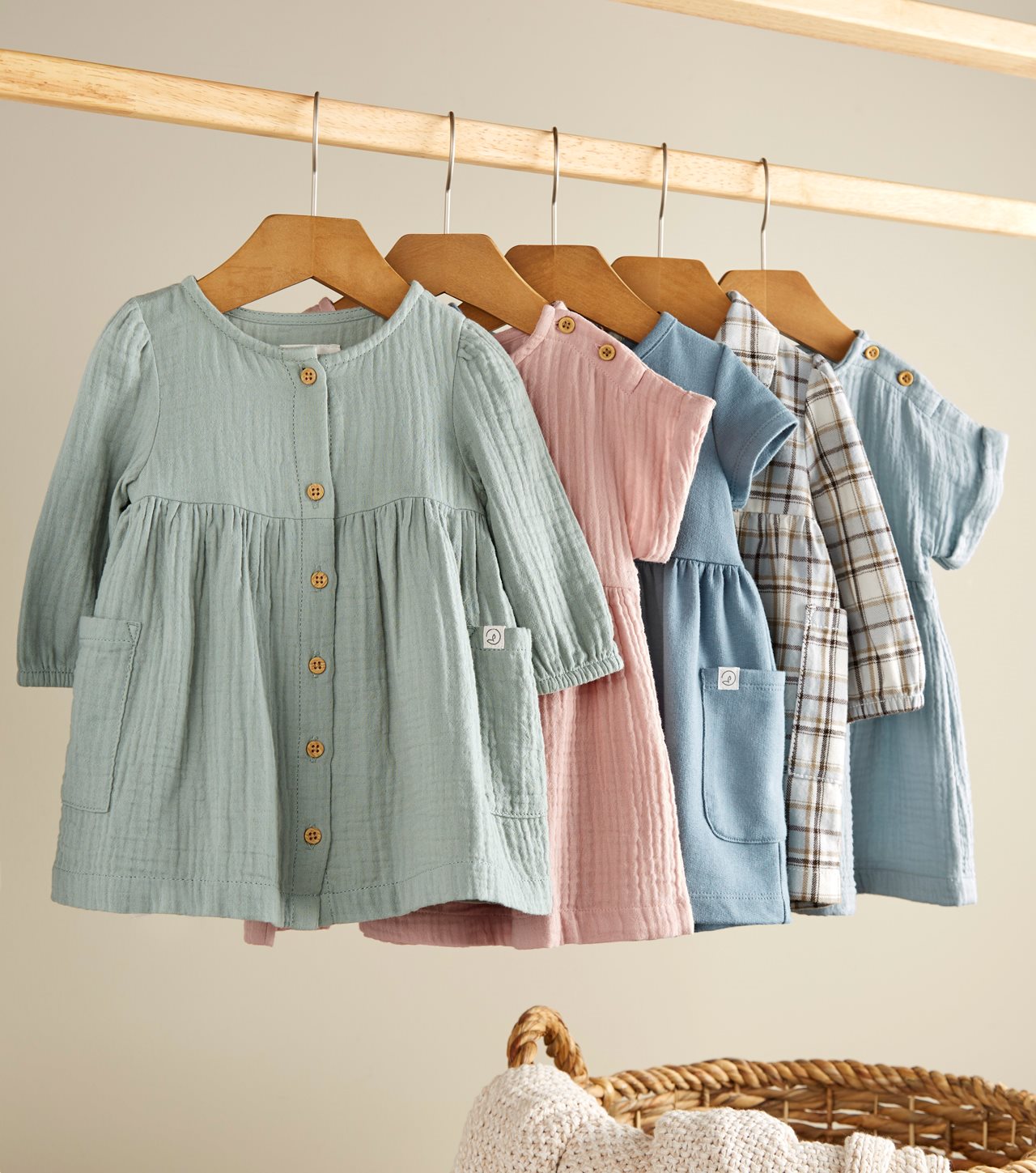 Five pretty little guaze dresses in a variety of colors hanging on hangers.