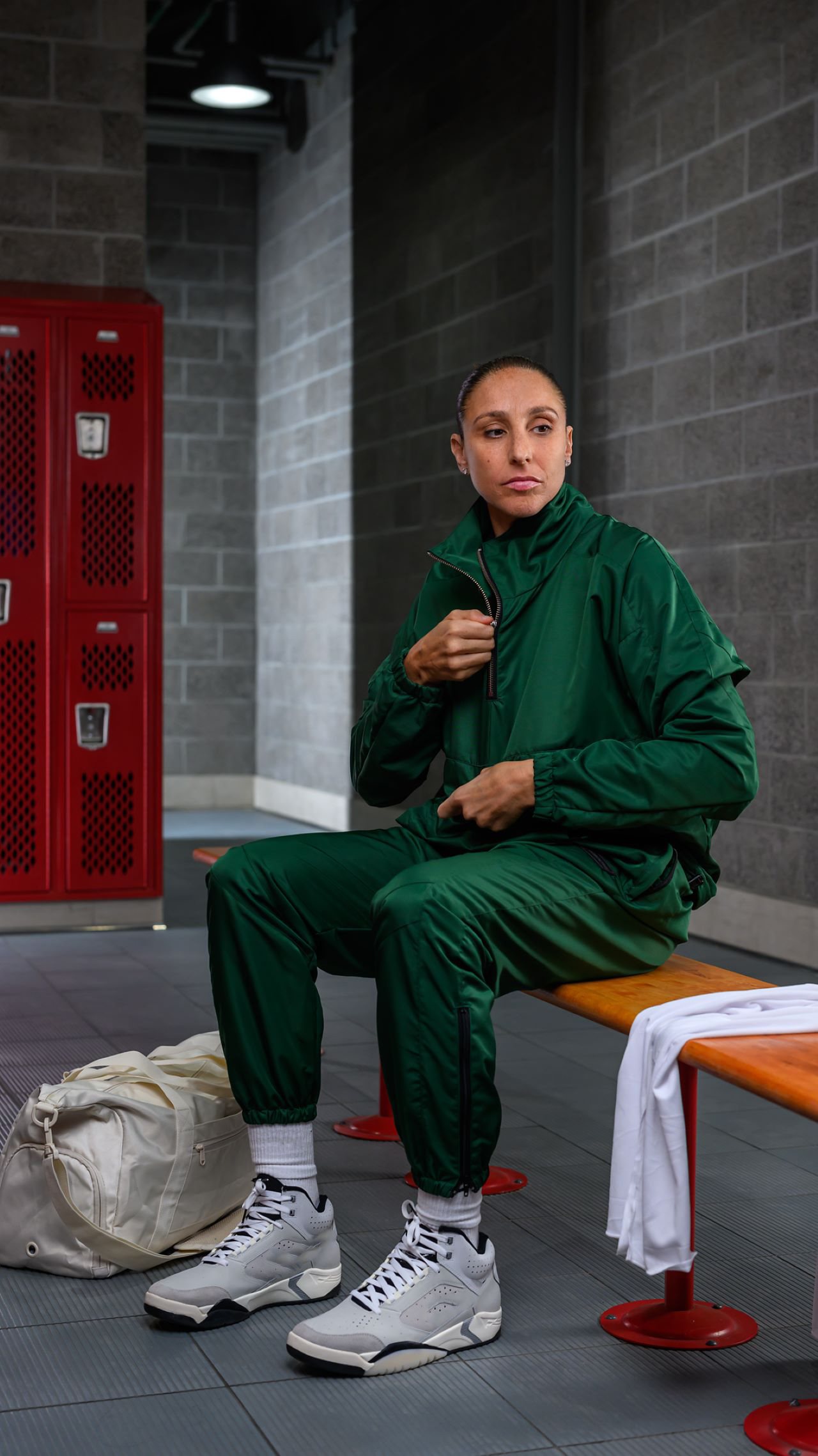 Diane wearing green workout suit sitting on a bench in a locker room.