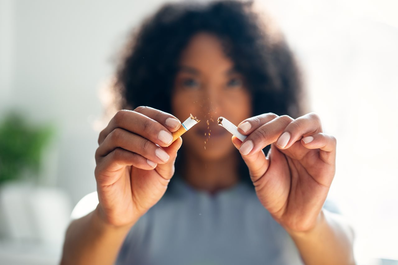 Dark haired woman wearing blue sweater and breaking a cigarette in half.