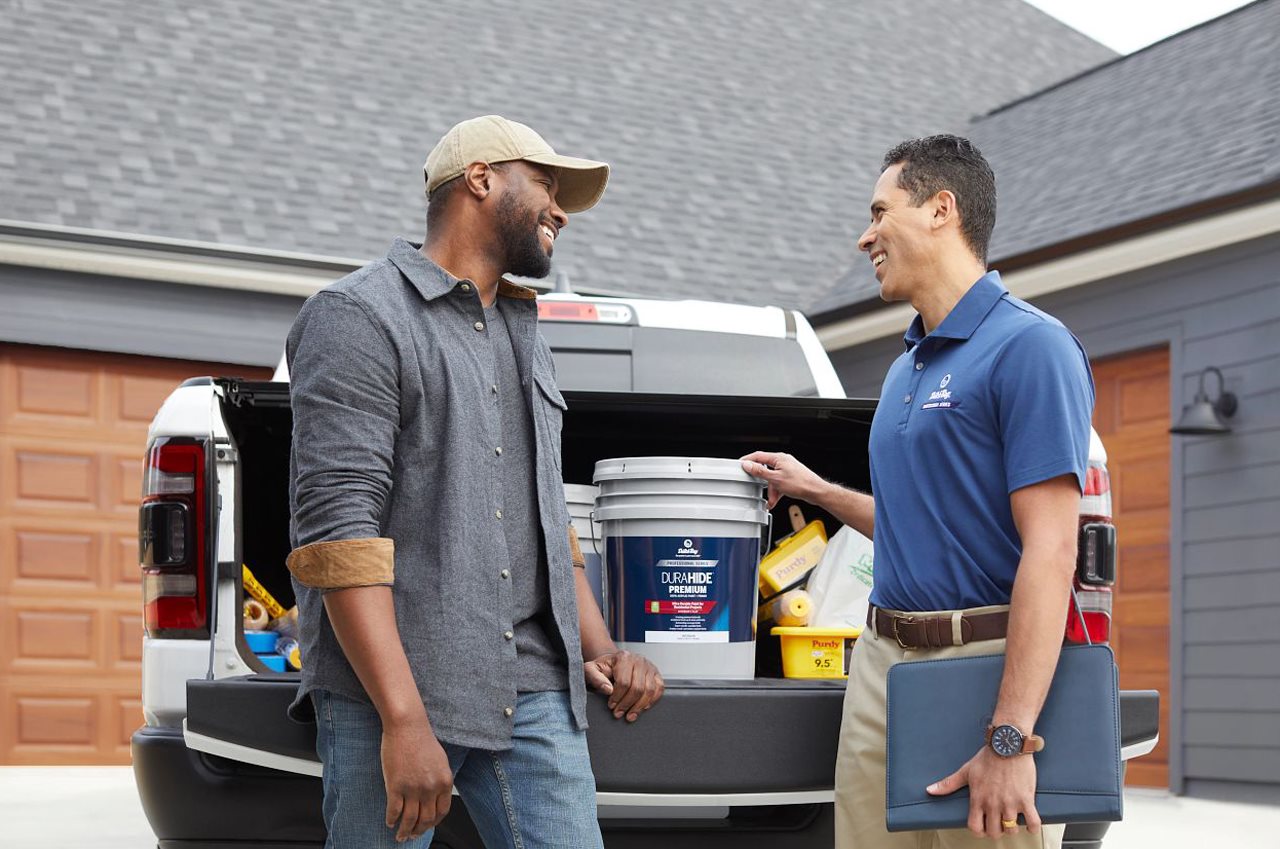 Homeowner and dutch boy professional referring to Dutch Boy paint on the tailgate of a truck in the driveway.