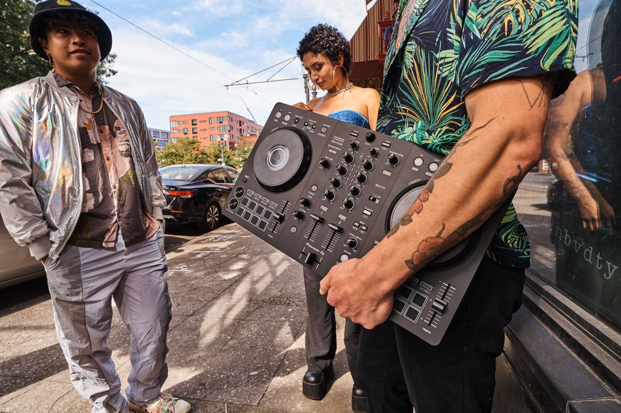 Three people standing outside of van with a DDJ-FLX4 from Pioneer.