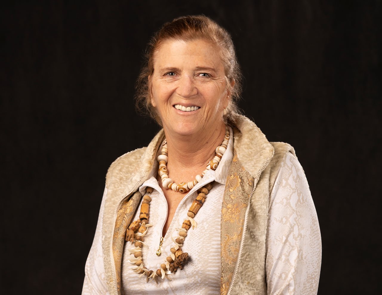 Smiling Allison wearing a light colored blouse with jacket and necklaces.