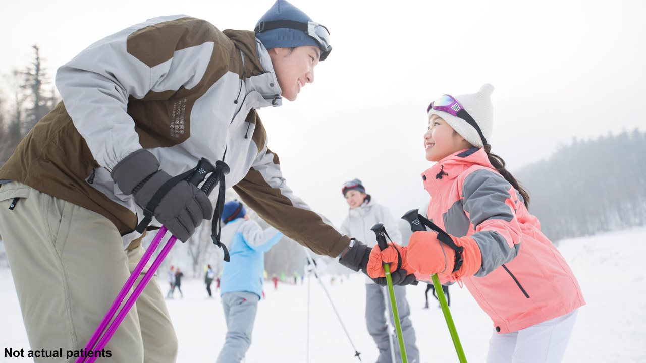 Dad and daughter wearing ski gear on a snowy hill.