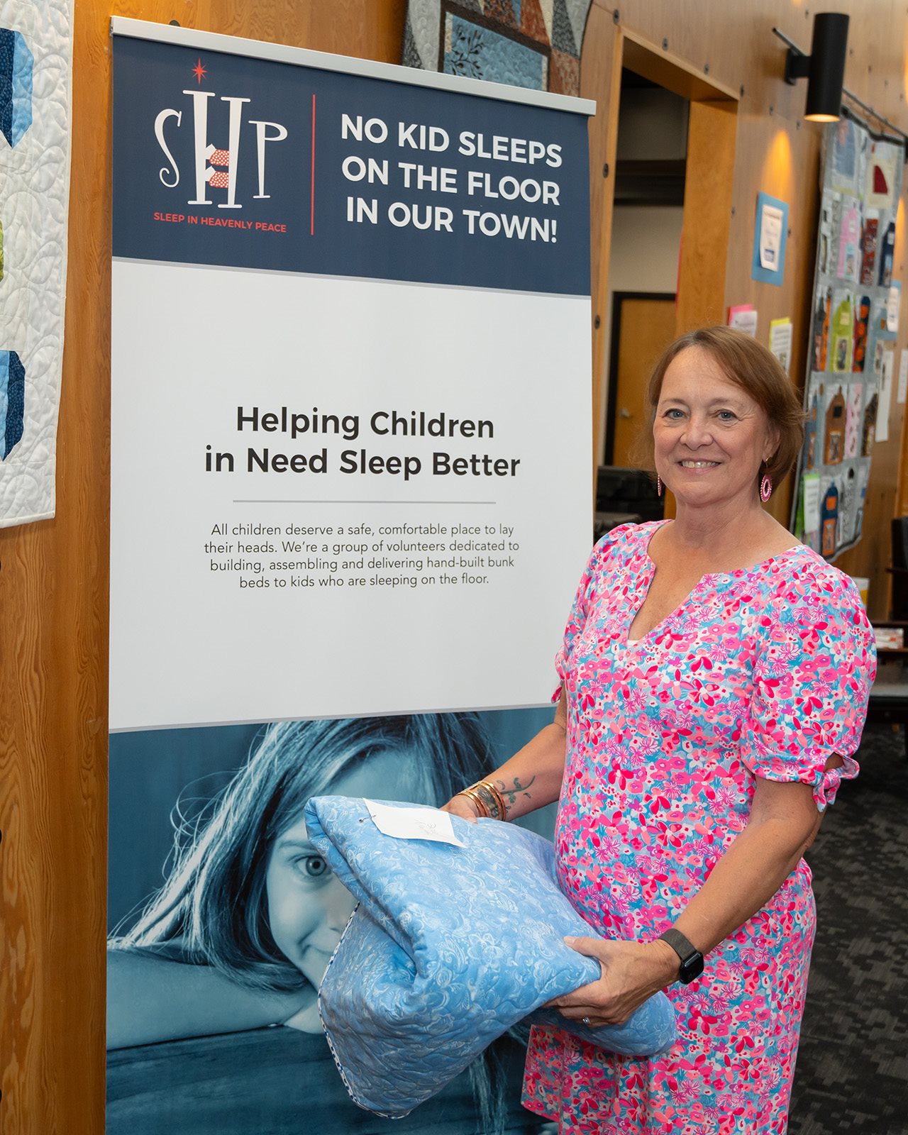 Jolene Fitch smiling while holding bedsheets in front of a banner reading 