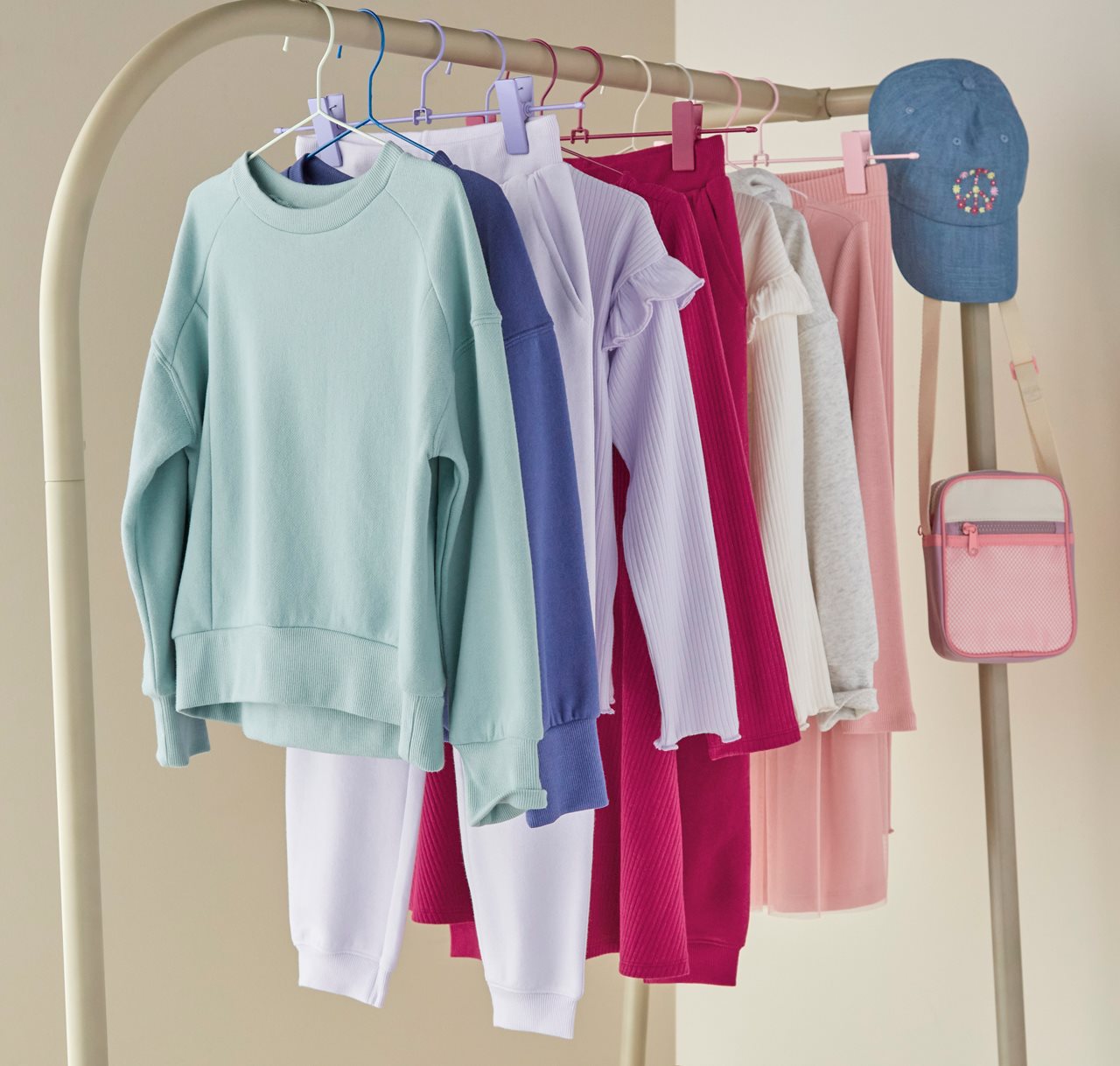 Pastle and brightly colored sweat sets hanging on a wardrobe pole with a cute peace symbol, jean baseball cap and pretty pink purse